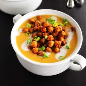 A square photo of a bowl of butternut squash soup with chickpeas and green onion on top.