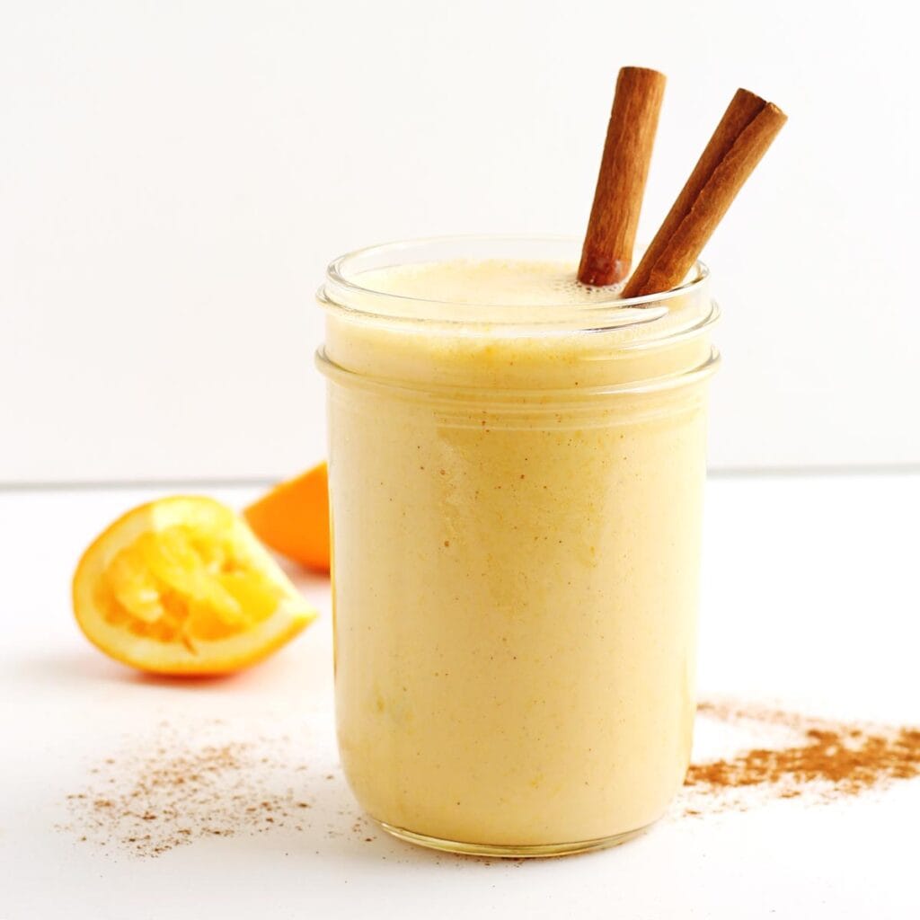 A square photo of an orange smoothie with cinnamon sticks.