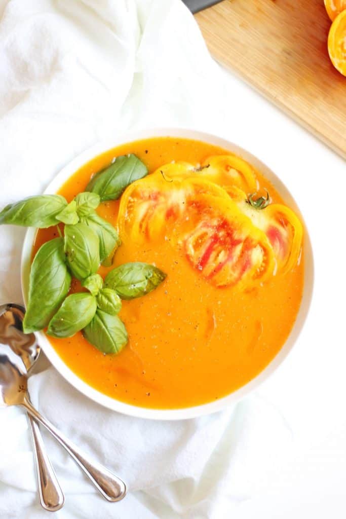 yellow tomato soup with fresh basil in a white bowl