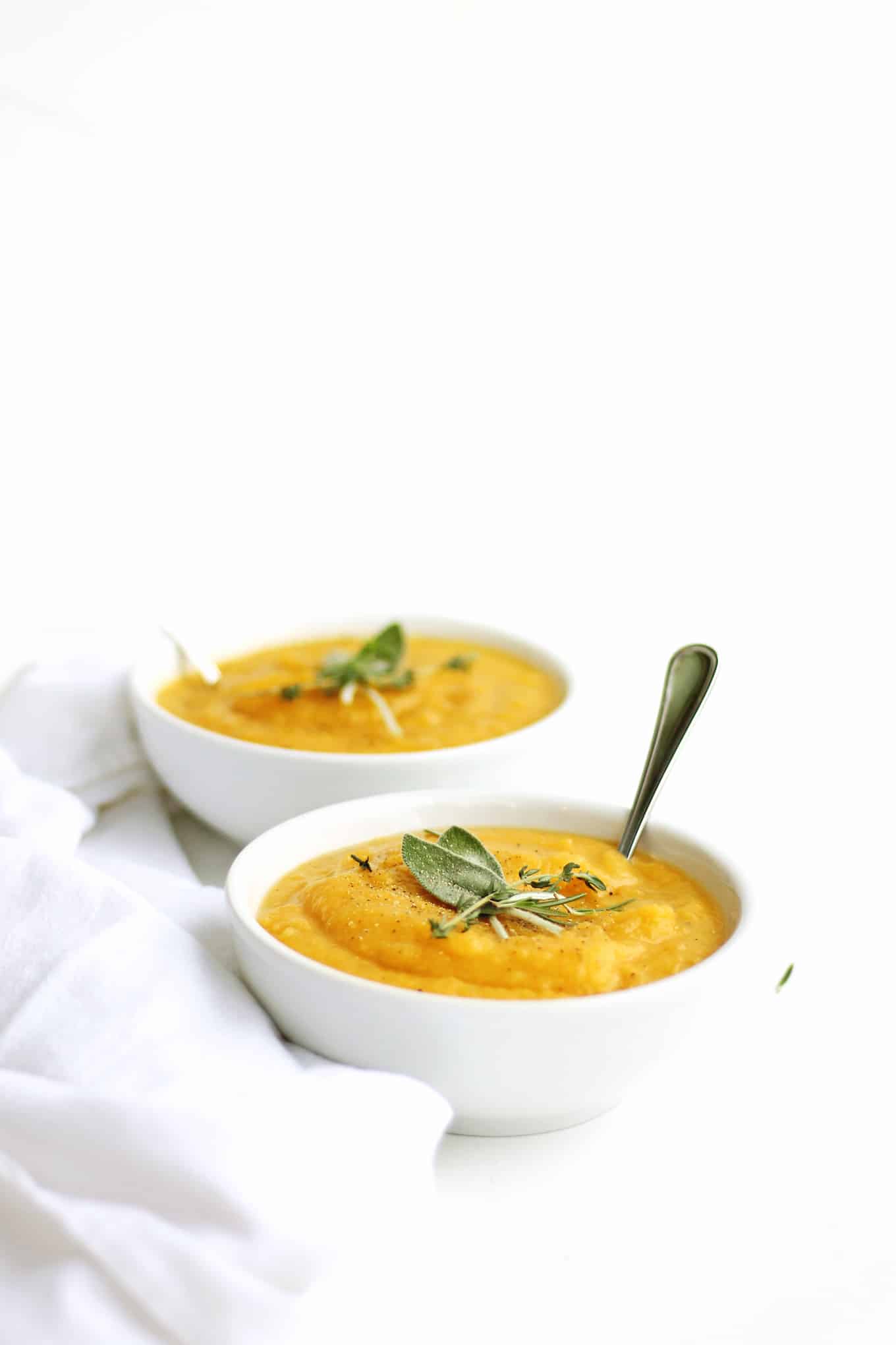 Butternut squash potato leek soup in a white bowl with herbs and a spoon
