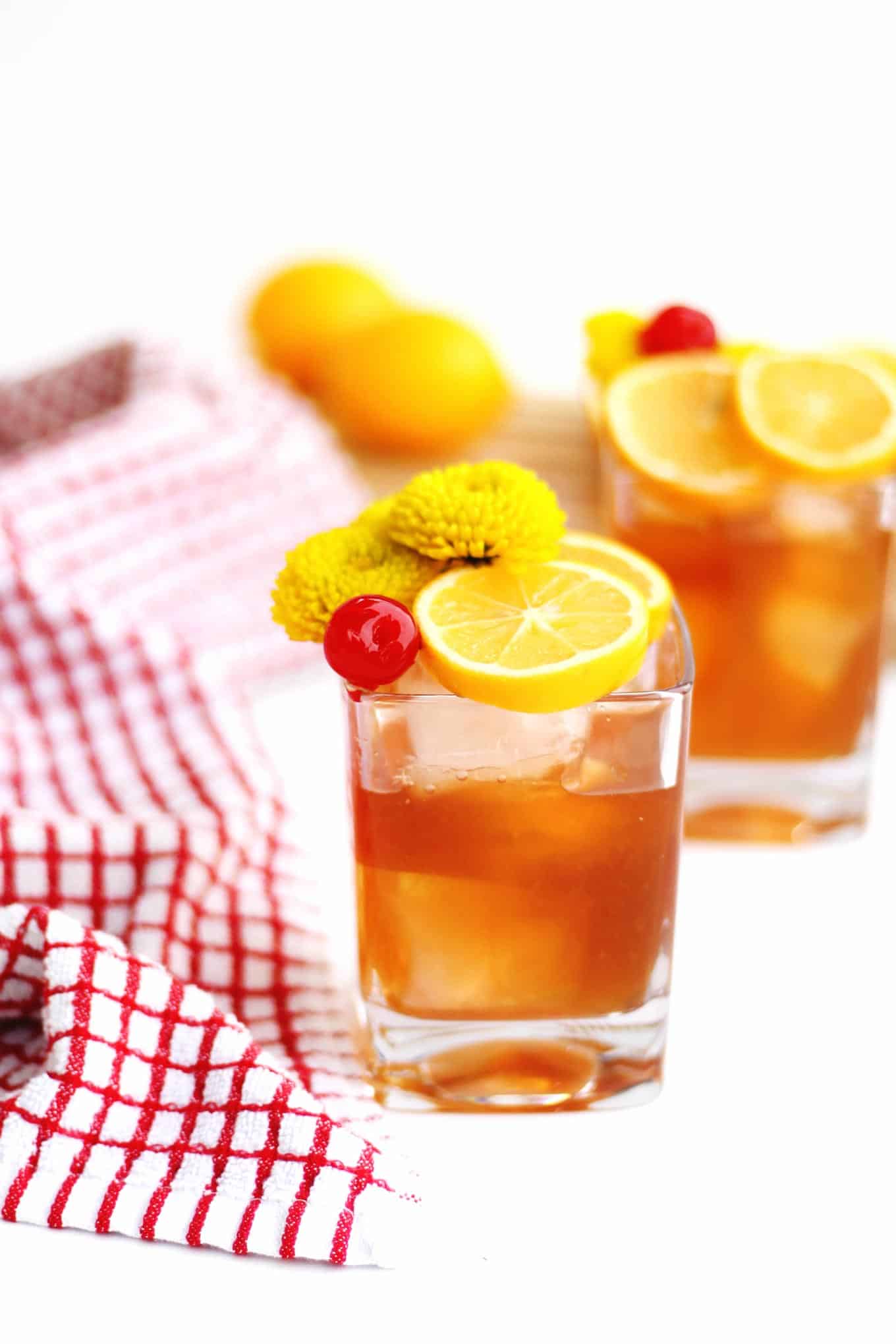 A photo of a lemon old fashioned with lemon slices, maraschino cherry, and yellow flowers on top.