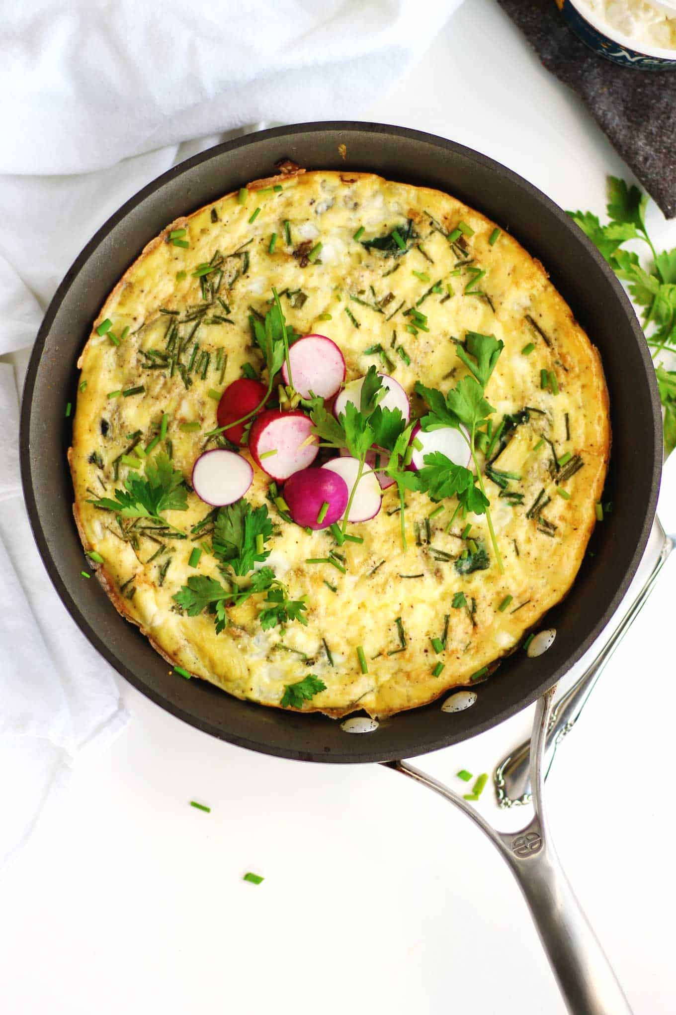 Spinach artichoke frittata in a pan with radishes on top