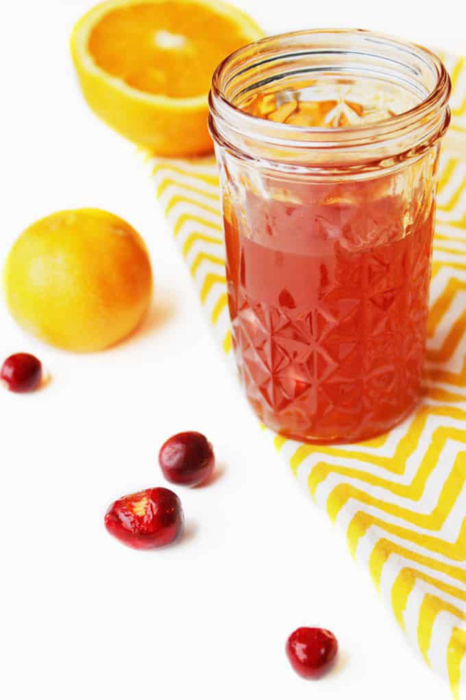 A photo of cranberry infused bourbon in a small glass jar with oranges on the side.