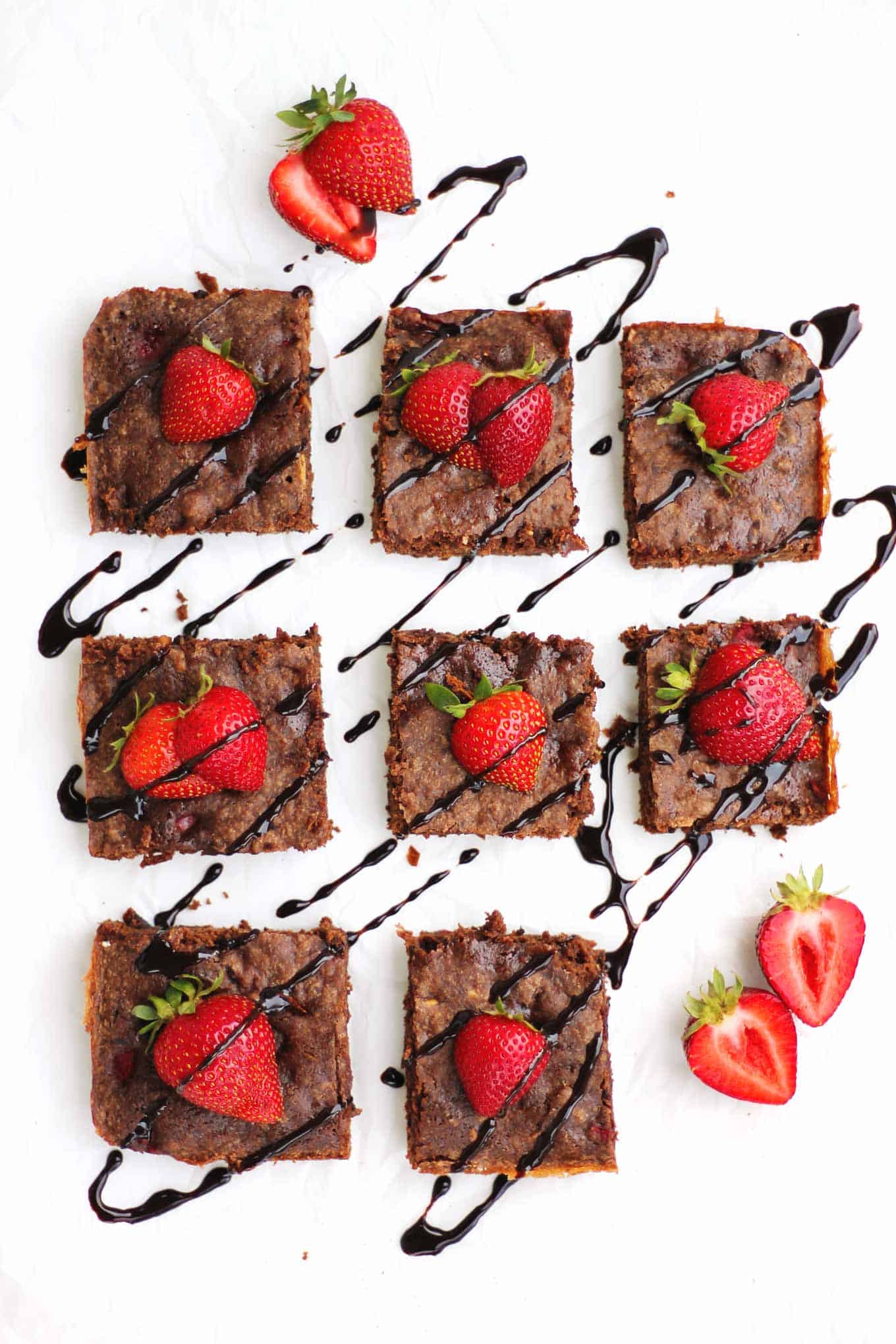 A picture of chocolate brownies with strawberries on top and drizzled with chocolate syrup.