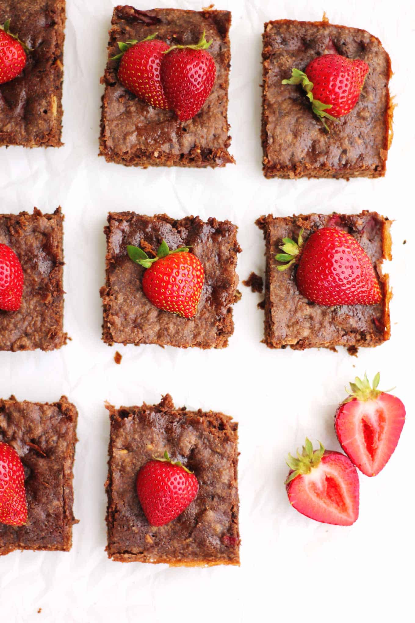 A picture of square cut brownies with halved fresh strawberries on top.