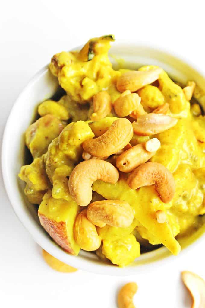 A close up photo of vegan cauliflower curry topped with roasted cashews in a white bowl.