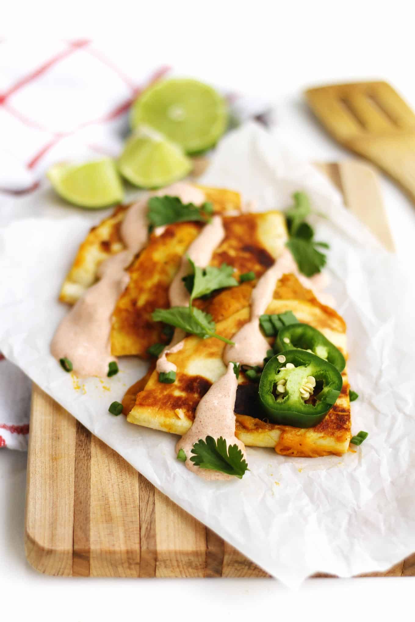 A photo of pumpkin quesadilla triangles overlapping and topped with jalapeno slices, cilantro, and sauce.