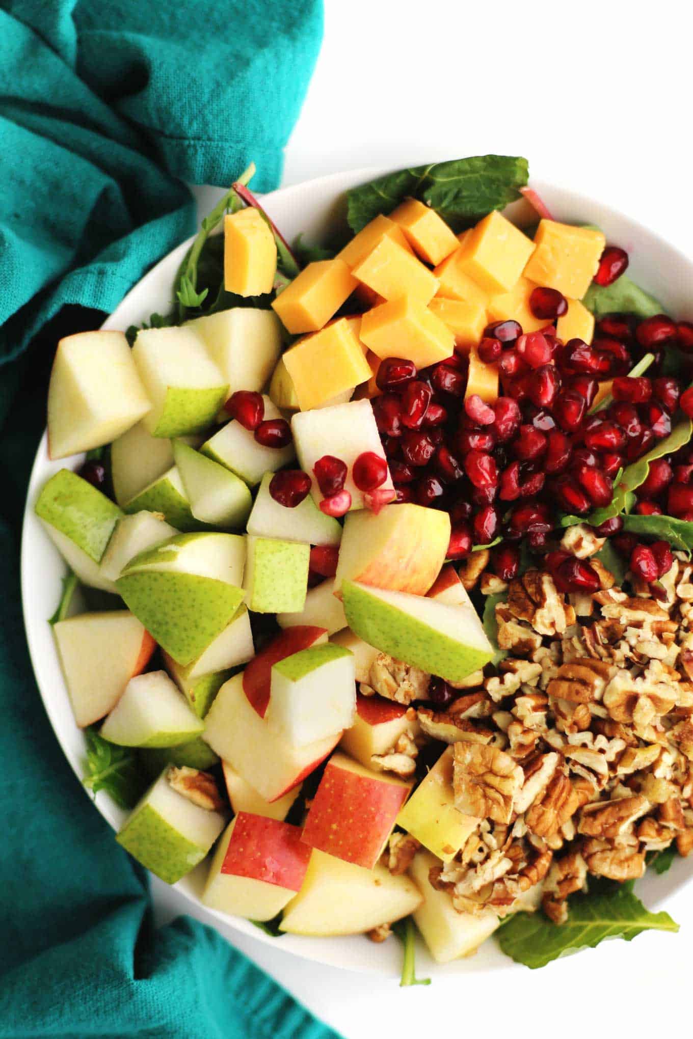 A close up photo of a salad with pears, apples, walnuts, cheddar cubes, and pomegranate arils.