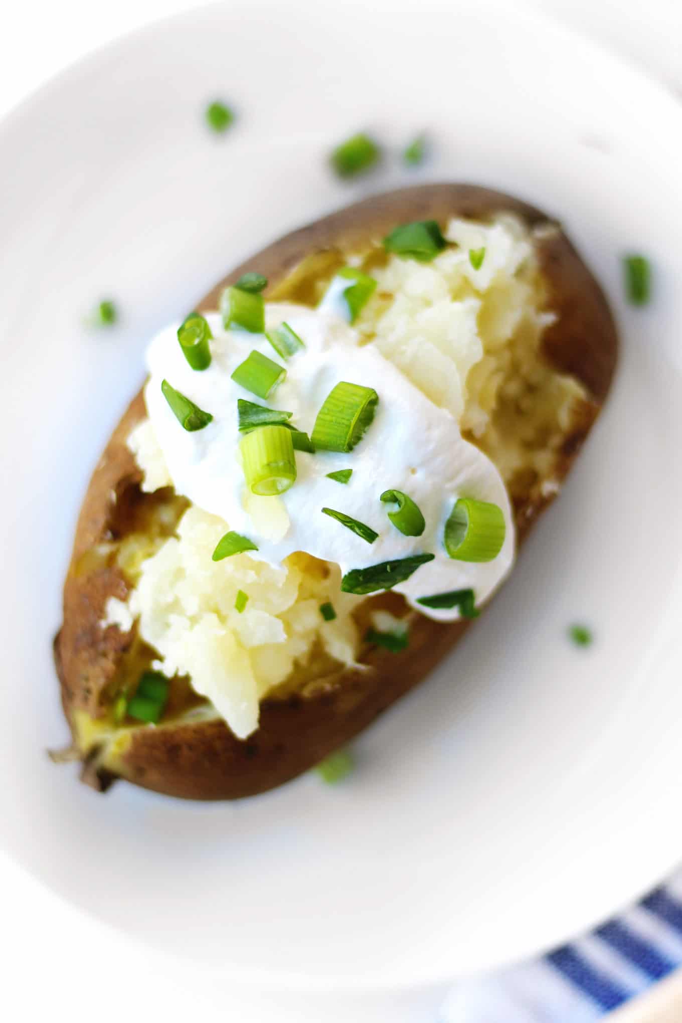An overhead photo of a baked potato cooked and topped with sour cream and green onion pieces.
