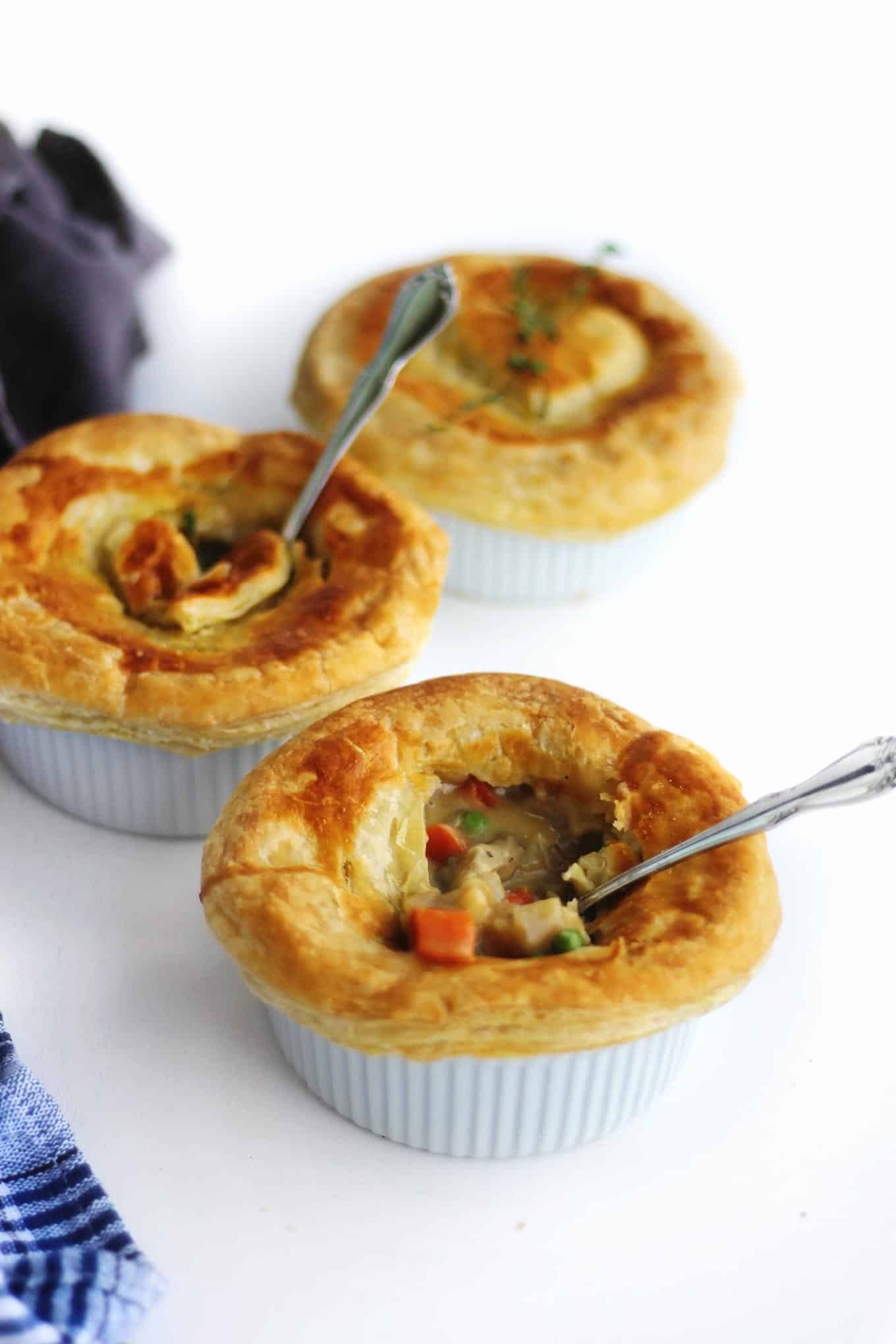 A photo of three pot pies in white ramekins one with a spoon in it.