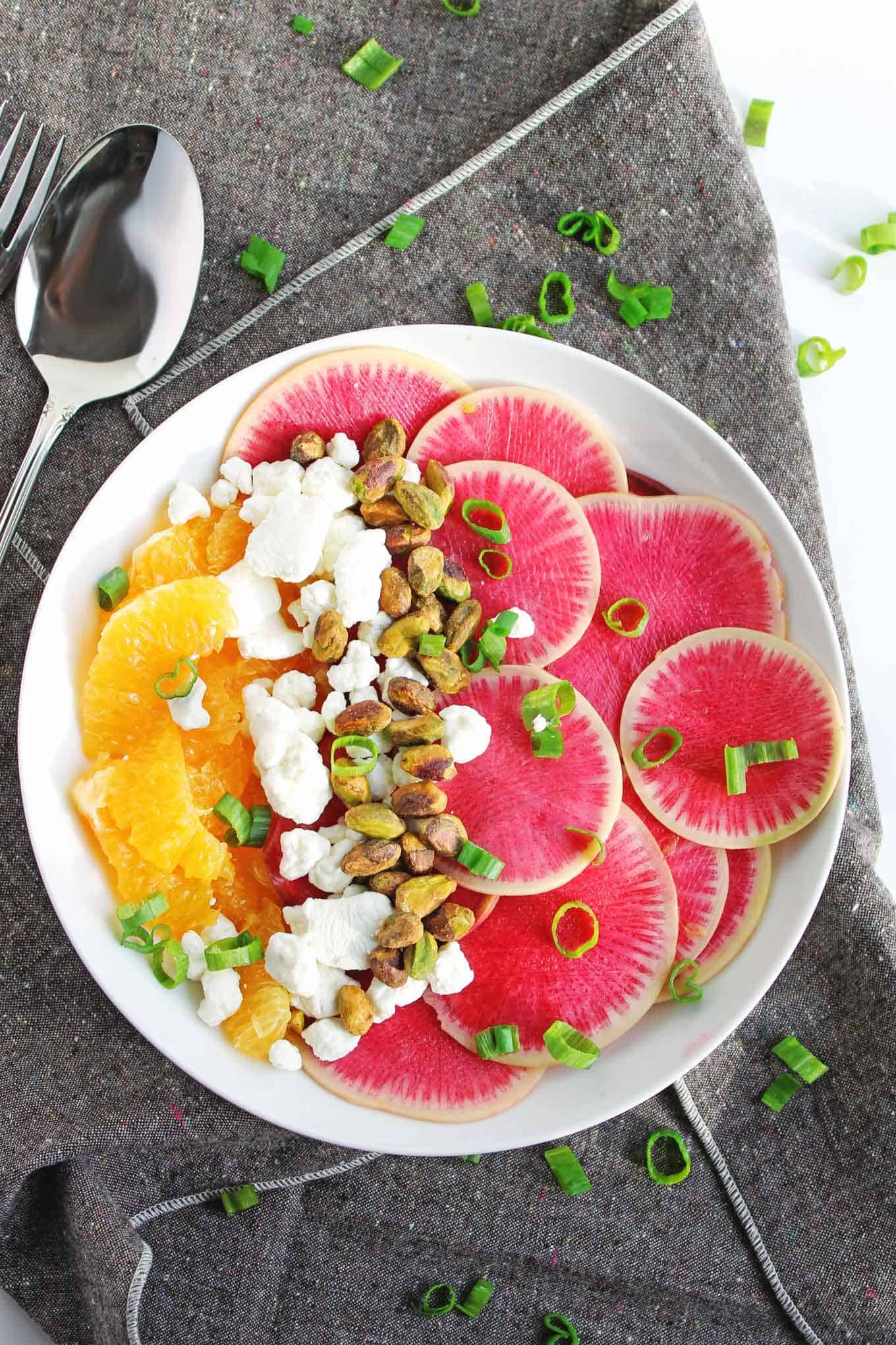 A photo of a watermelon radish salad with oranges, goat cheese, and pistachios.