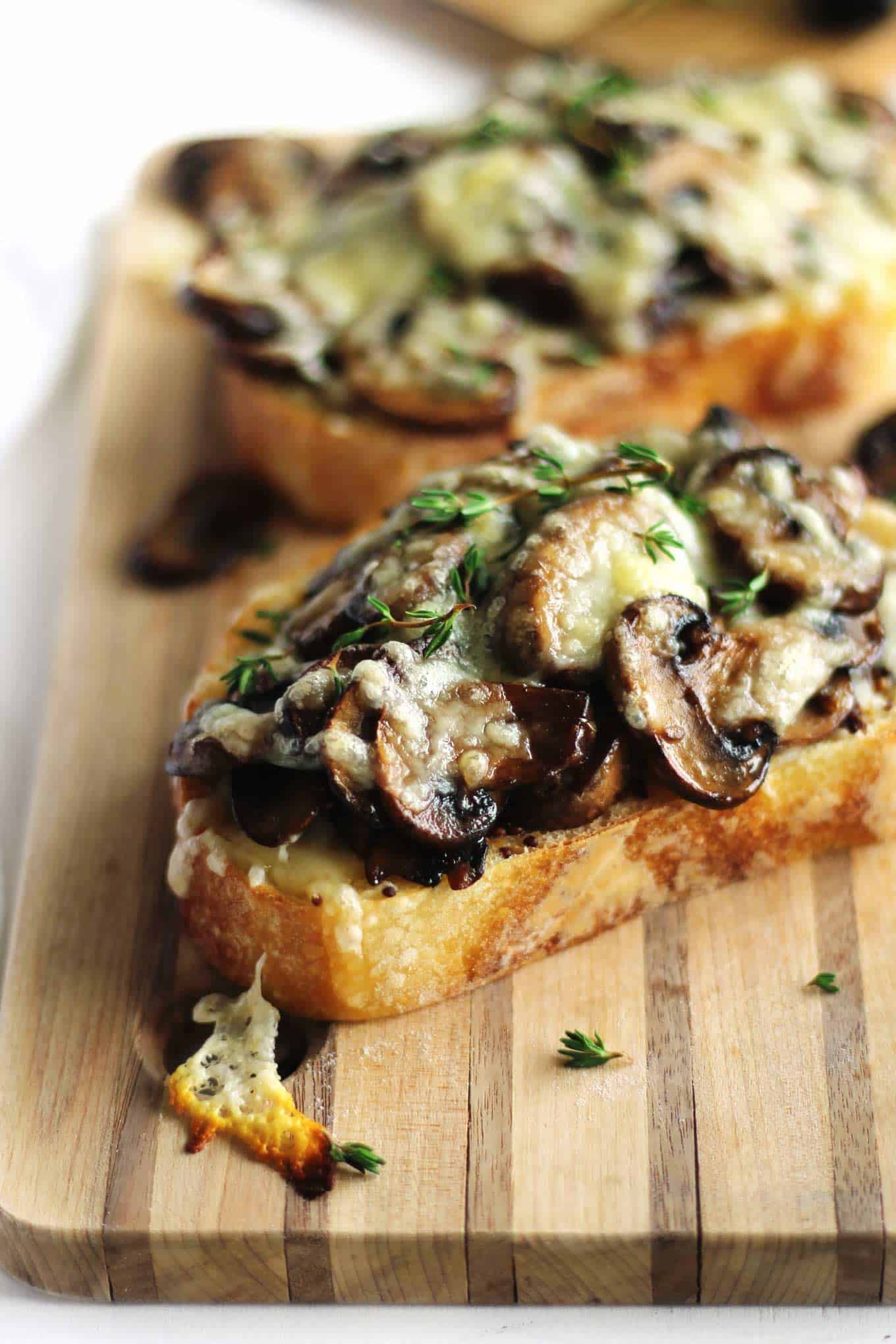 A photo of sauteed mushrooms on toast with broiled cheese and fresh thyme on top.