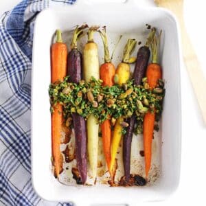 A square photo of roasted rainbow carrots with a pistachio herb relish on top.