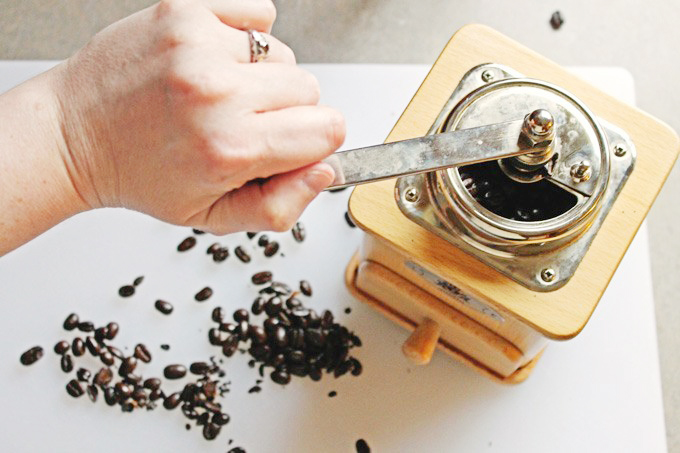 A picture of a hand grinding coffee beans in an old fashioned coffee grinder.
