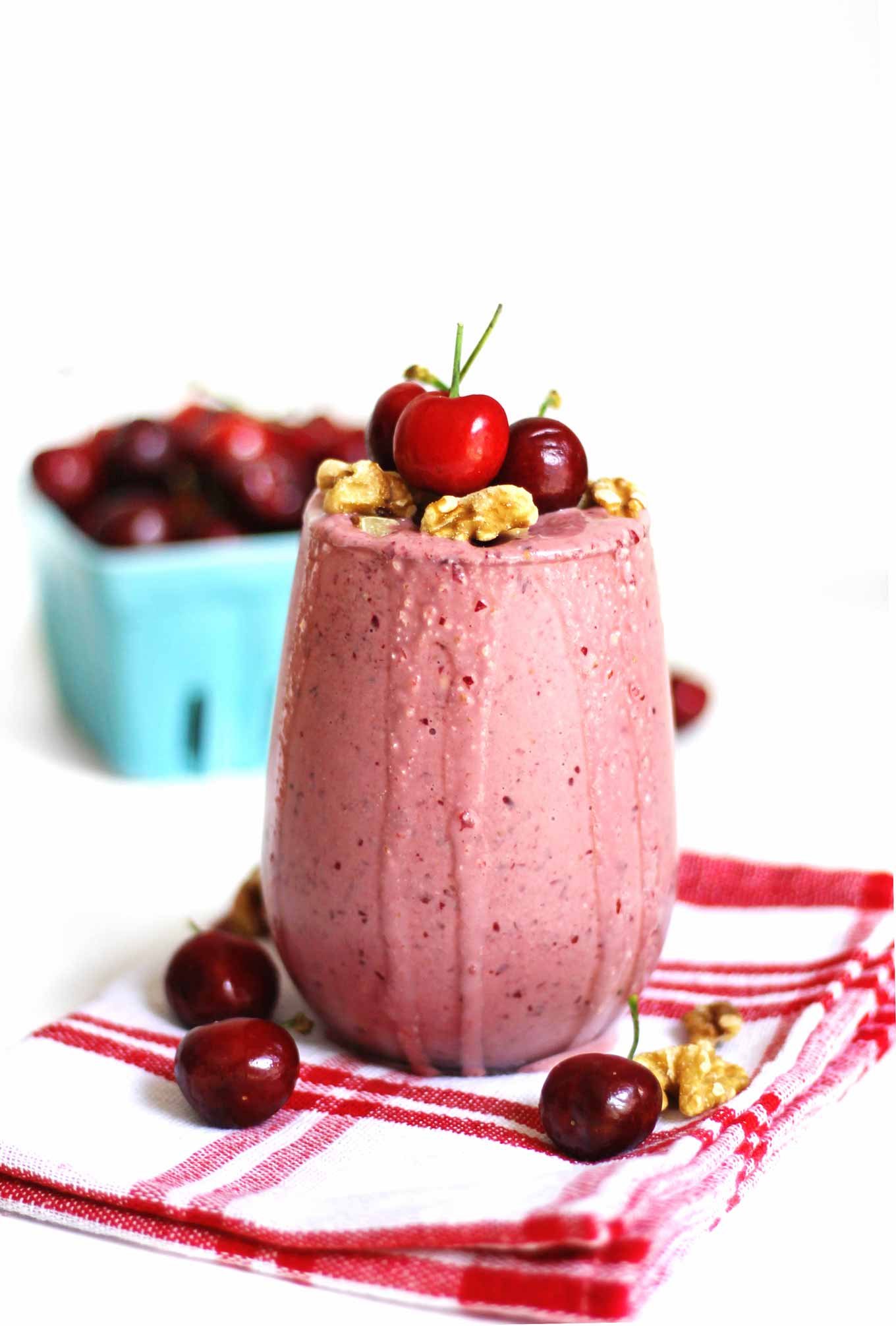A photo of a cherry smoothie with fresh cherries and walnuts on top.