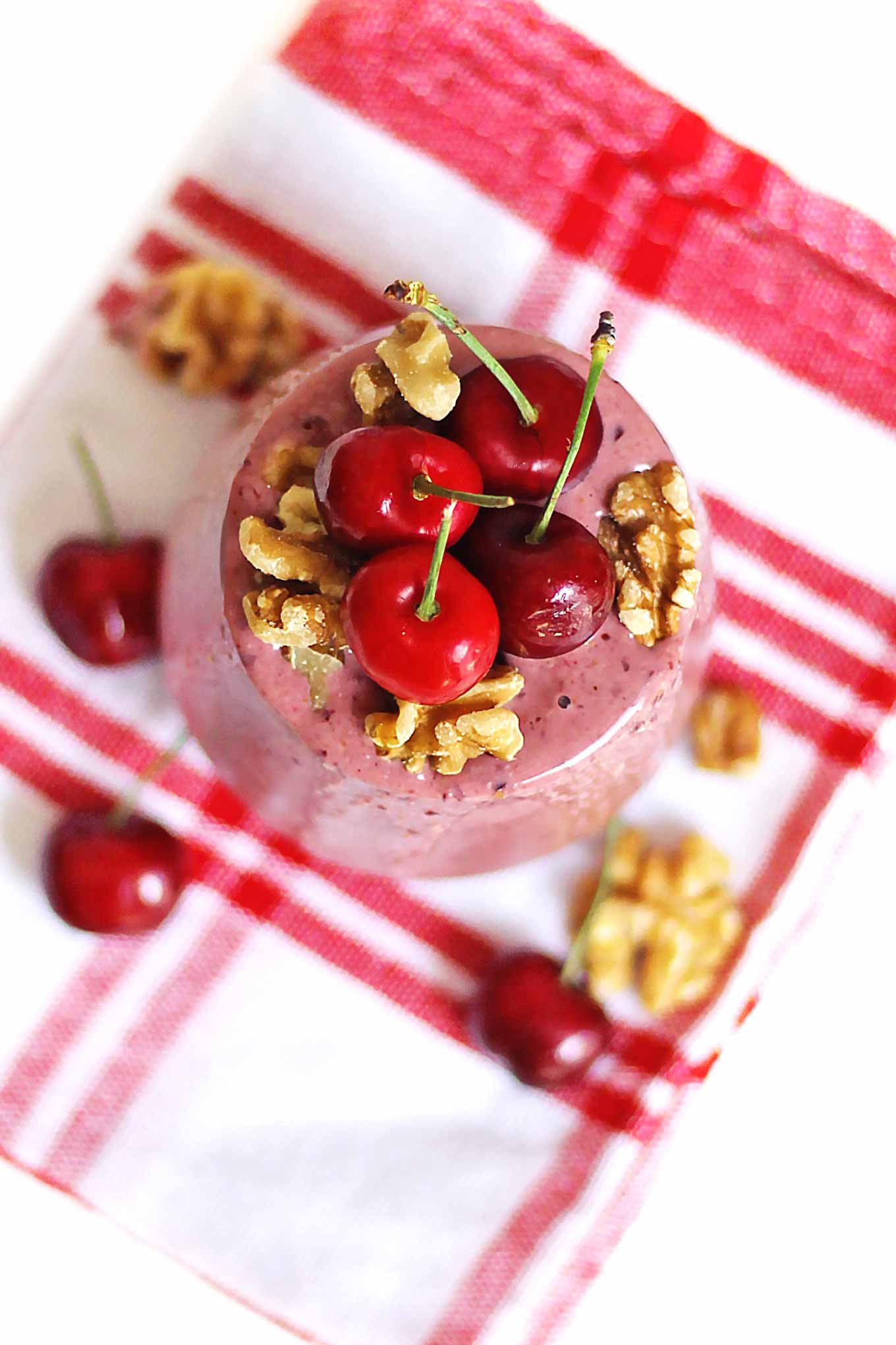 A picture of the top of a cherry smoothie with yogurt, fresh cherries, and walnuts on top.