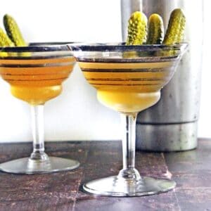 A square photo of two dill pickle martini cocktails.