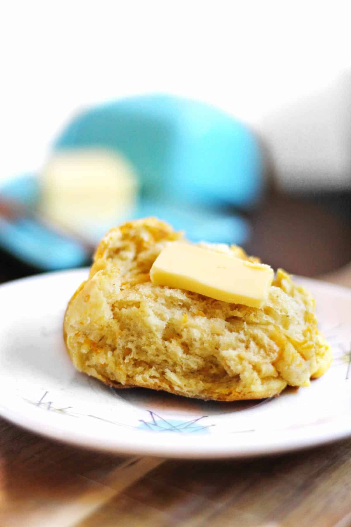 A photo of a dinner roll cut in half with butter on top on a white plate.