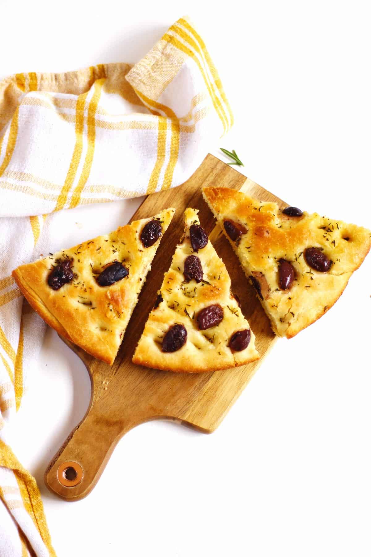 A photo of three triangle slices of olive rosemary focaccia bread on a wooden cutting board.
