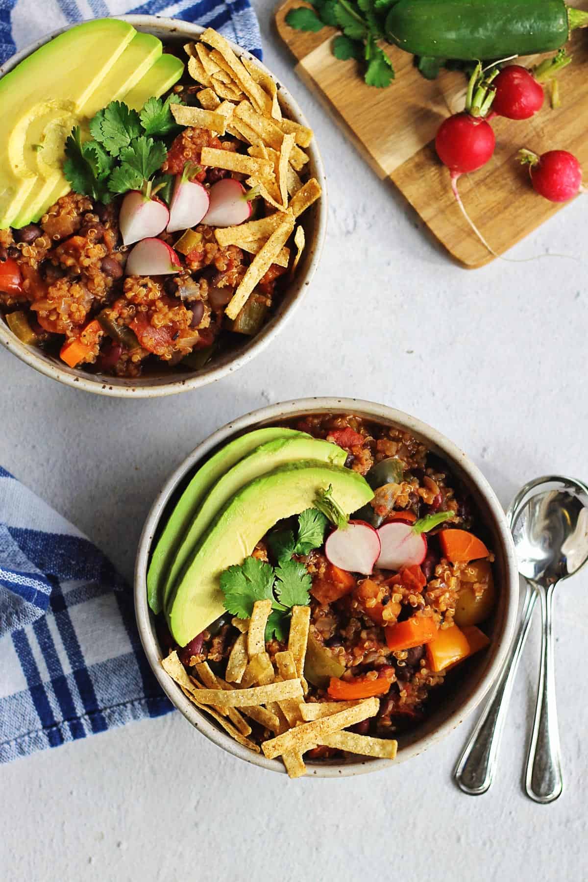 A photo of two bowls of quinoa chili with avocado slices, cilantro, tortilla strips, and radish halves.
