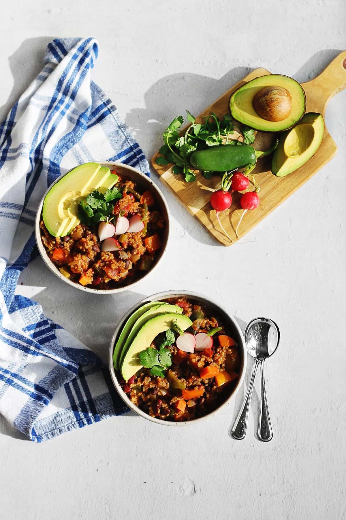A photo of two bowls of vegetarian chili with quinoa and avocado slices on top.