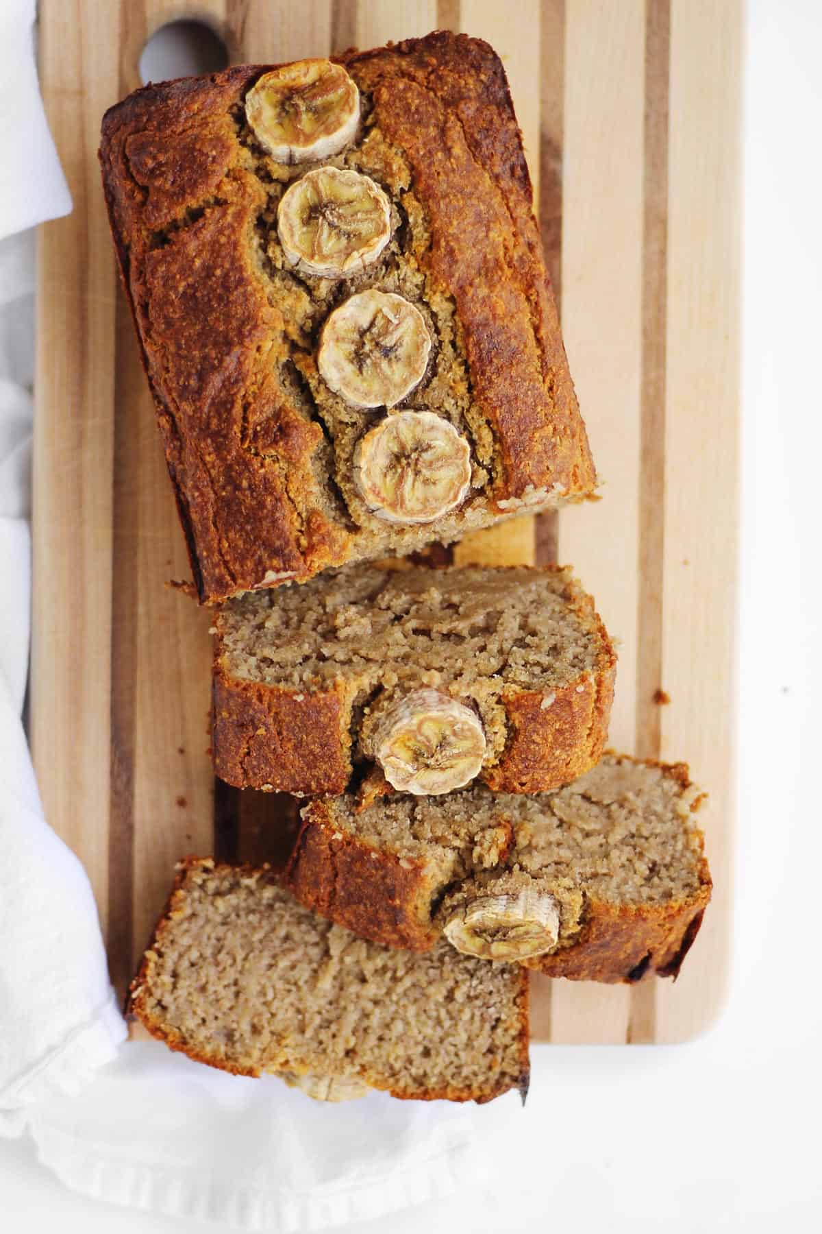 A photo of a loaf of oat flour banana bread with half of the loaf sliced on a cutting board.