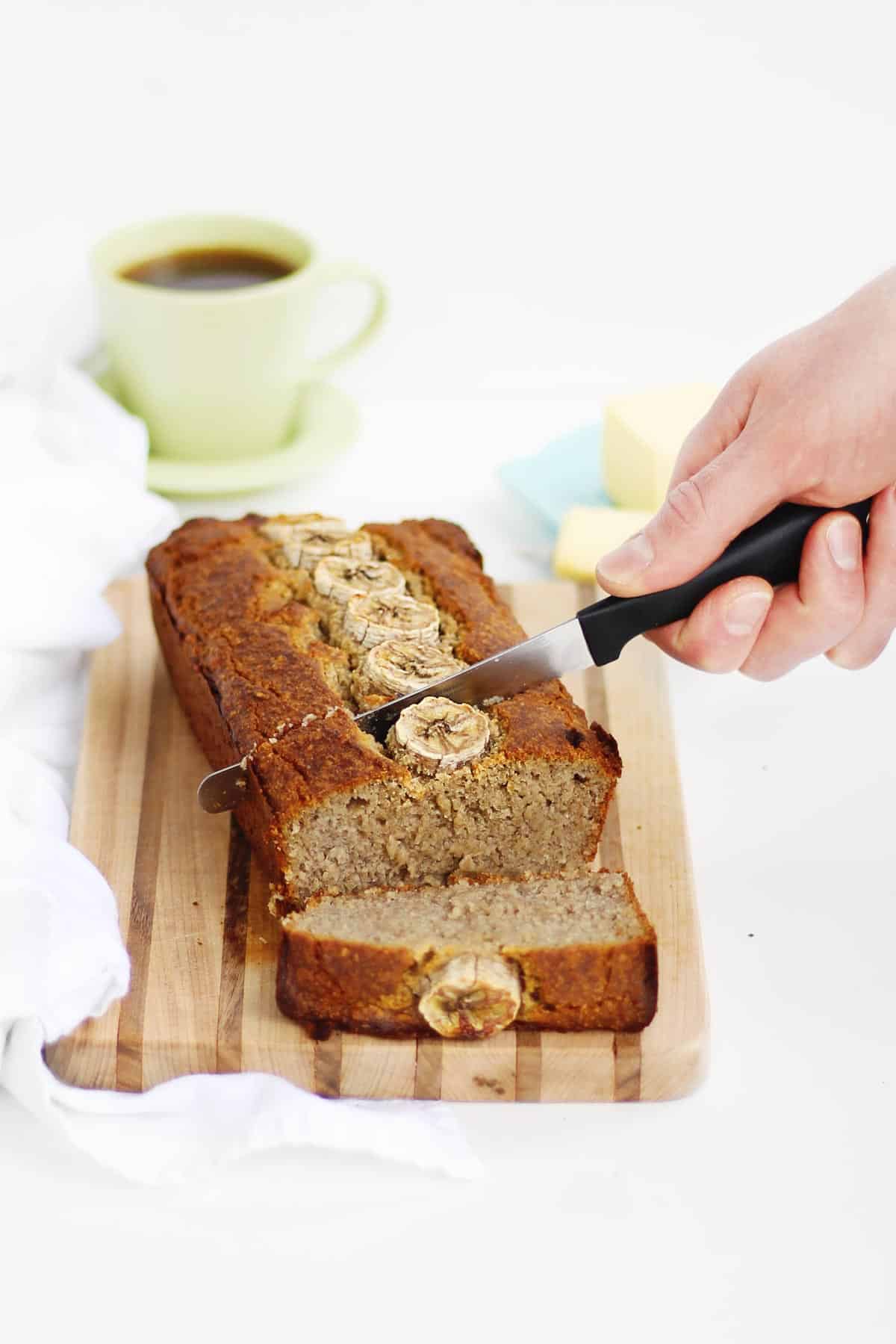 A photo of slicing a loaf of banana bread with a small knife.