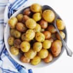 A square photo of Instant Pot baby potatoes in a white bowl with a spoon holding one potato.