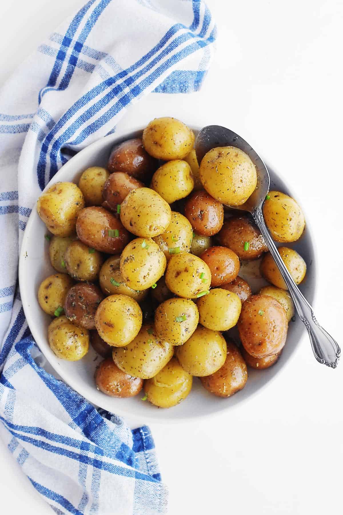 A photo of Instant Pot baby potatoes in a white bowl next to a blue and white plaid napkin.