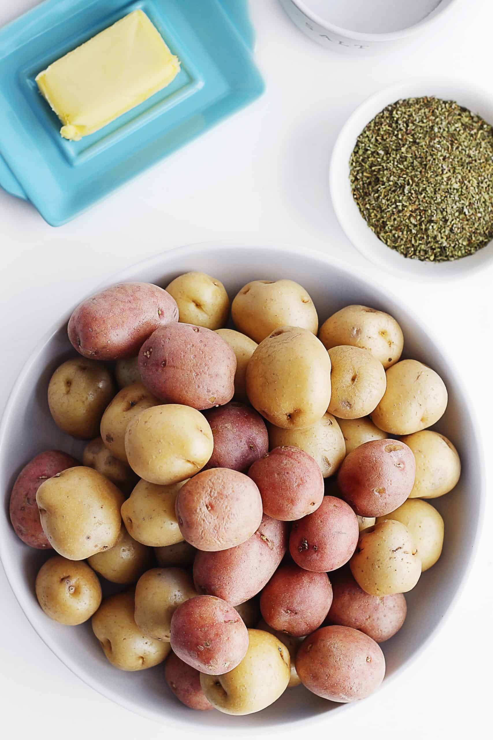 A picture of a bowl of raw baby potatoes next to Italian seasoning and butter.