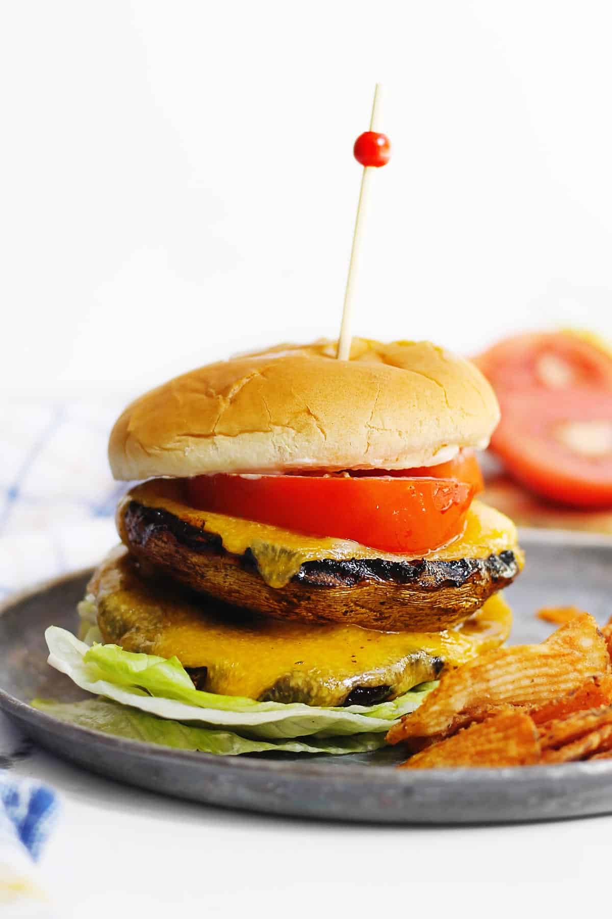 A photo of a double portobello mushroom burger with tomato and cheddar on a metal plate.