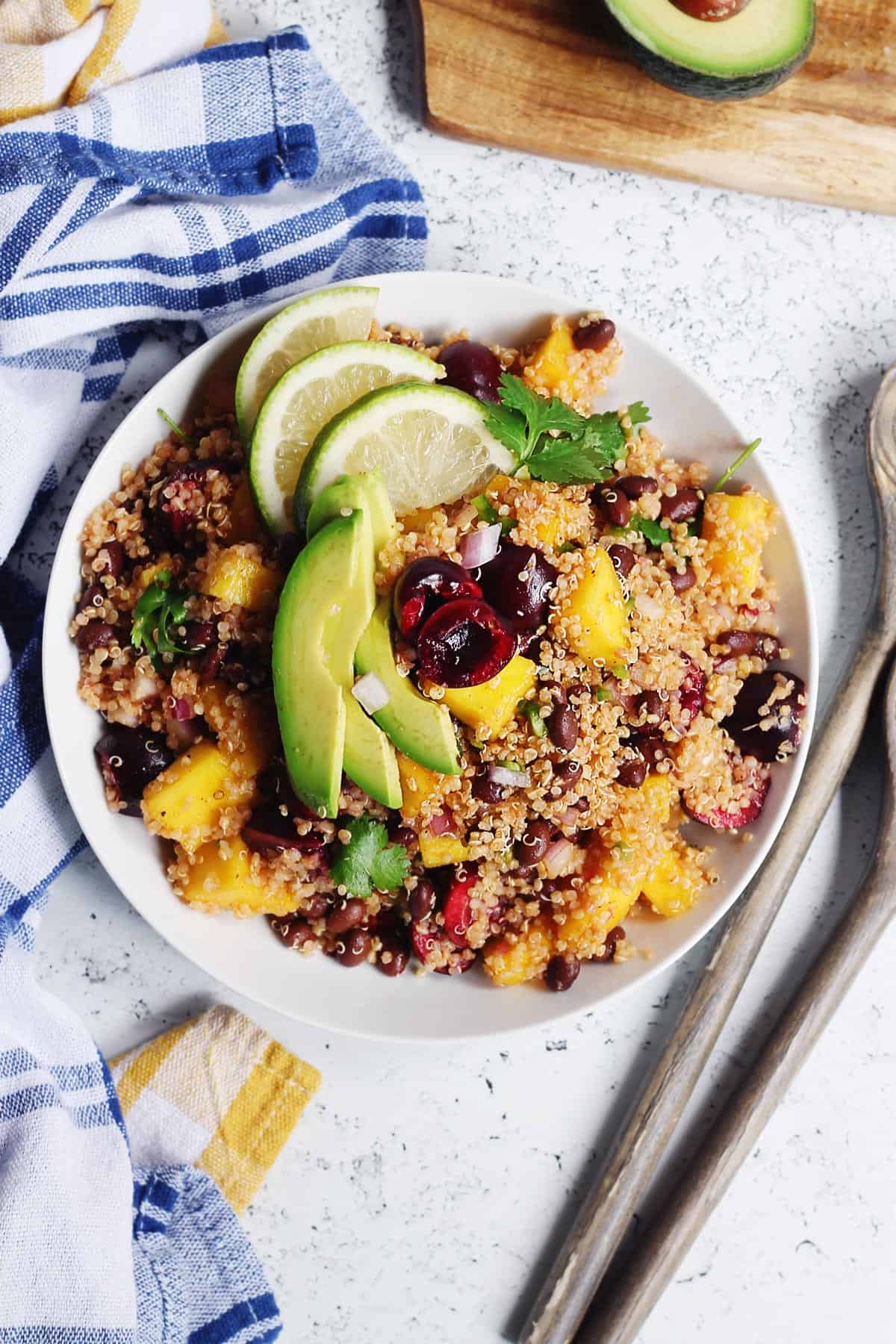 Black bean quinoa salad with avocado, cherries, and lime in a white bowl