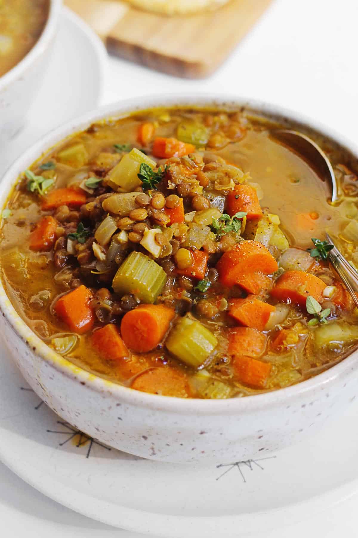 A close up picture of pumpkin lentil soup with lots of vegetables and a spoon in it.