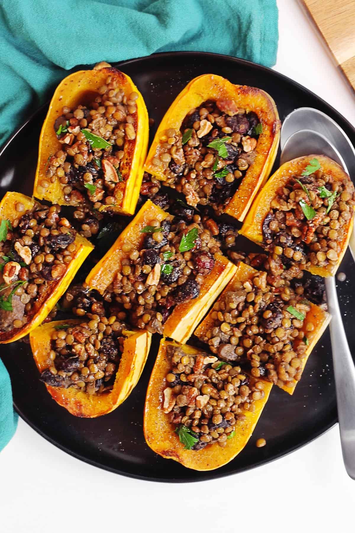 A photo of delicata squash stuffed with a lentil cranberry pecan mixture on a black plate with two spoons.