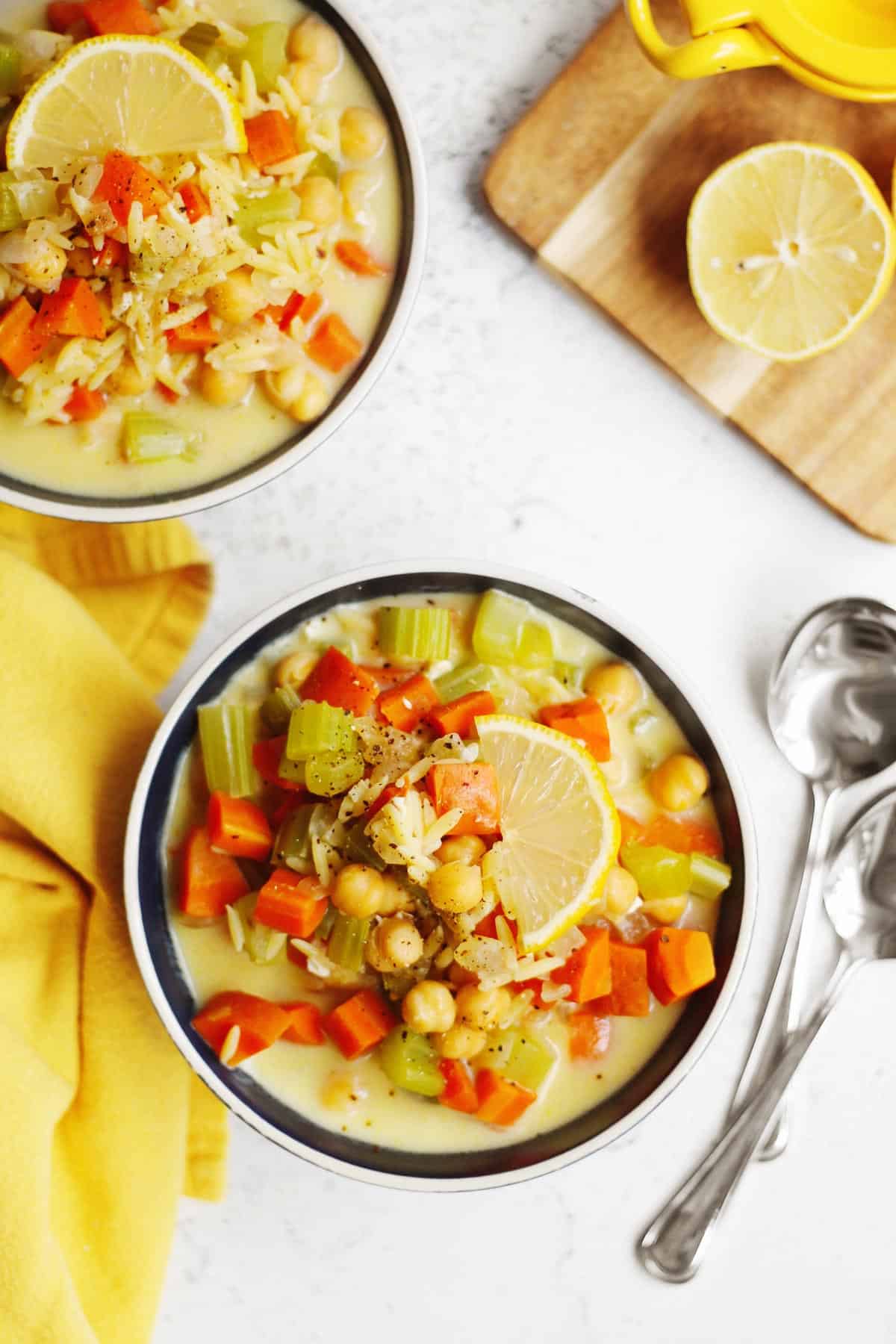 A photo of a bowl of chickpea lemon orzo soup with a lemon slice on top.