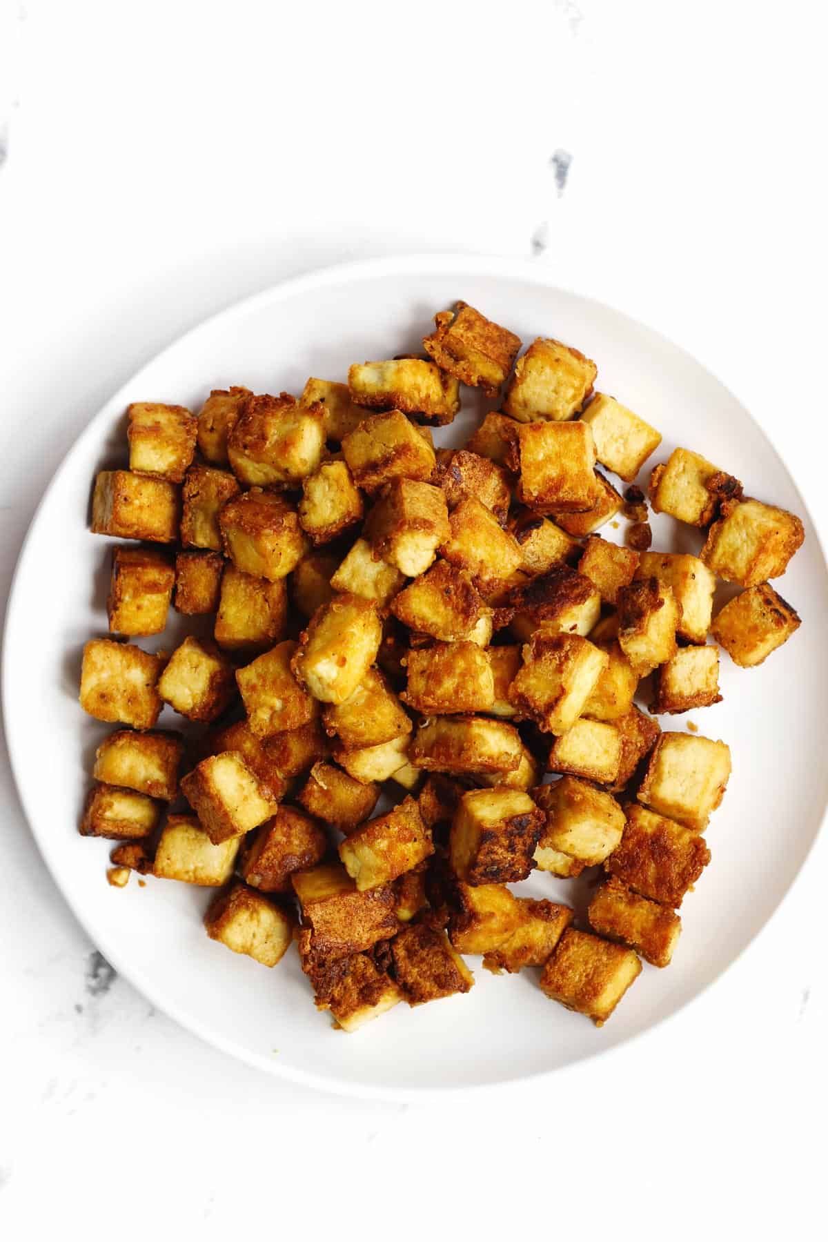 A photo of crispy tofu cubes on a white plate.