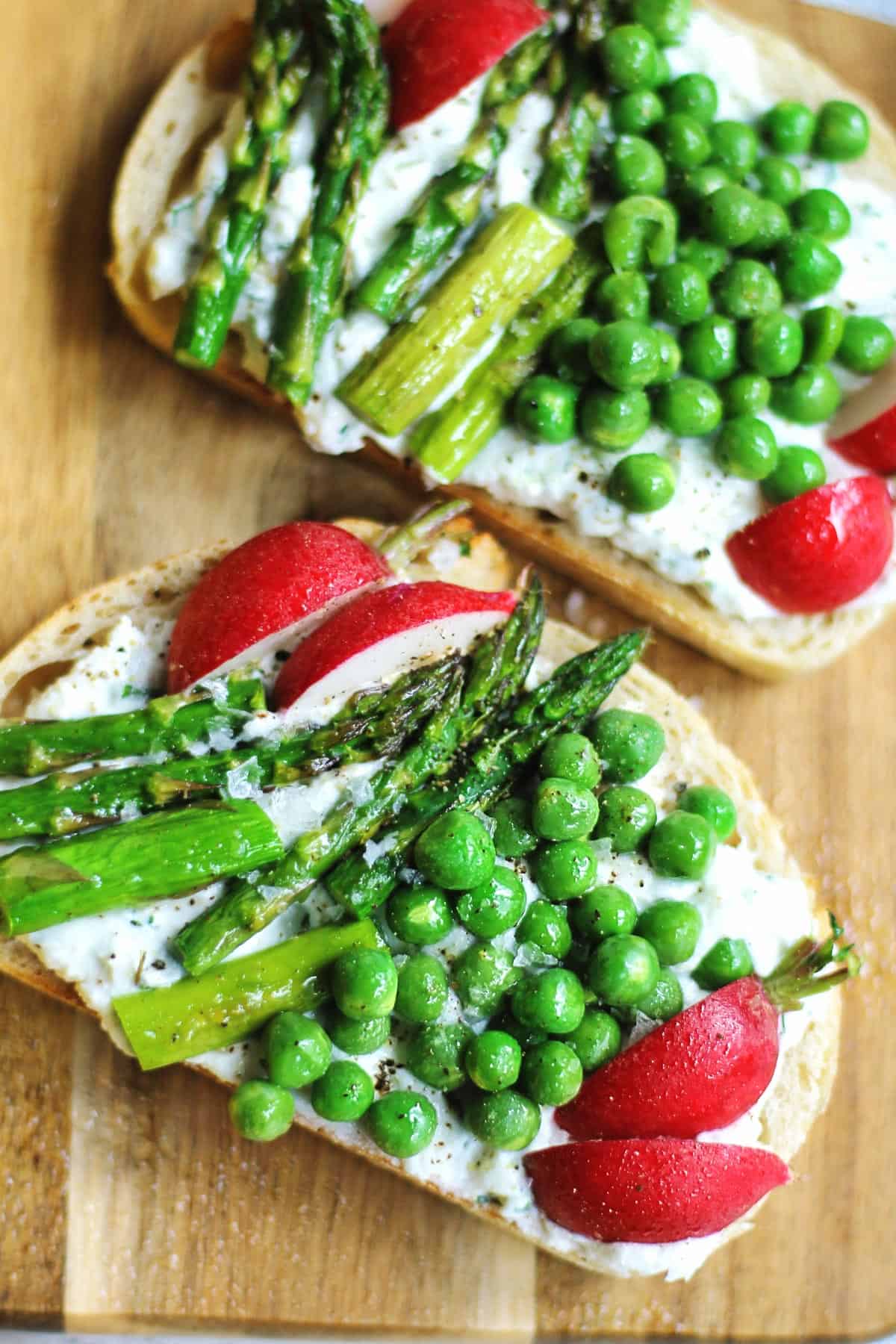 A photo of two spring veggie goat cheese toasts on a cutting board.