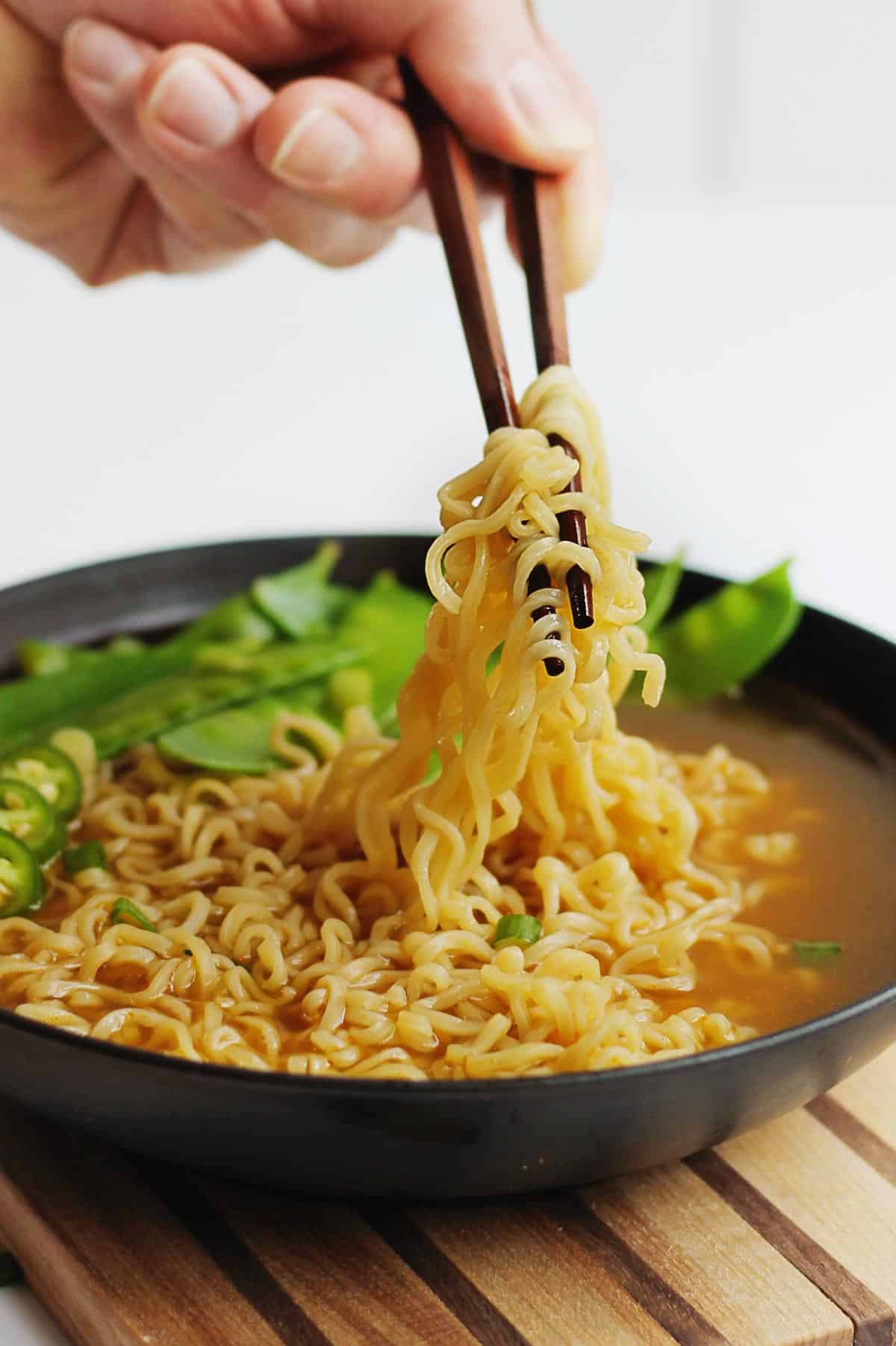 A picture of scooping up ramen noodles with chopsticks in a black bowl.