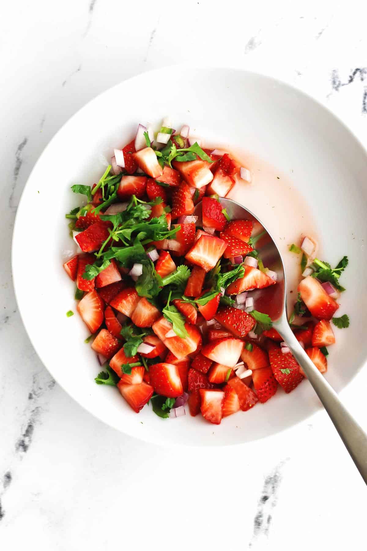 Strawberry pico de gallo in a white bowl with a silver spoon