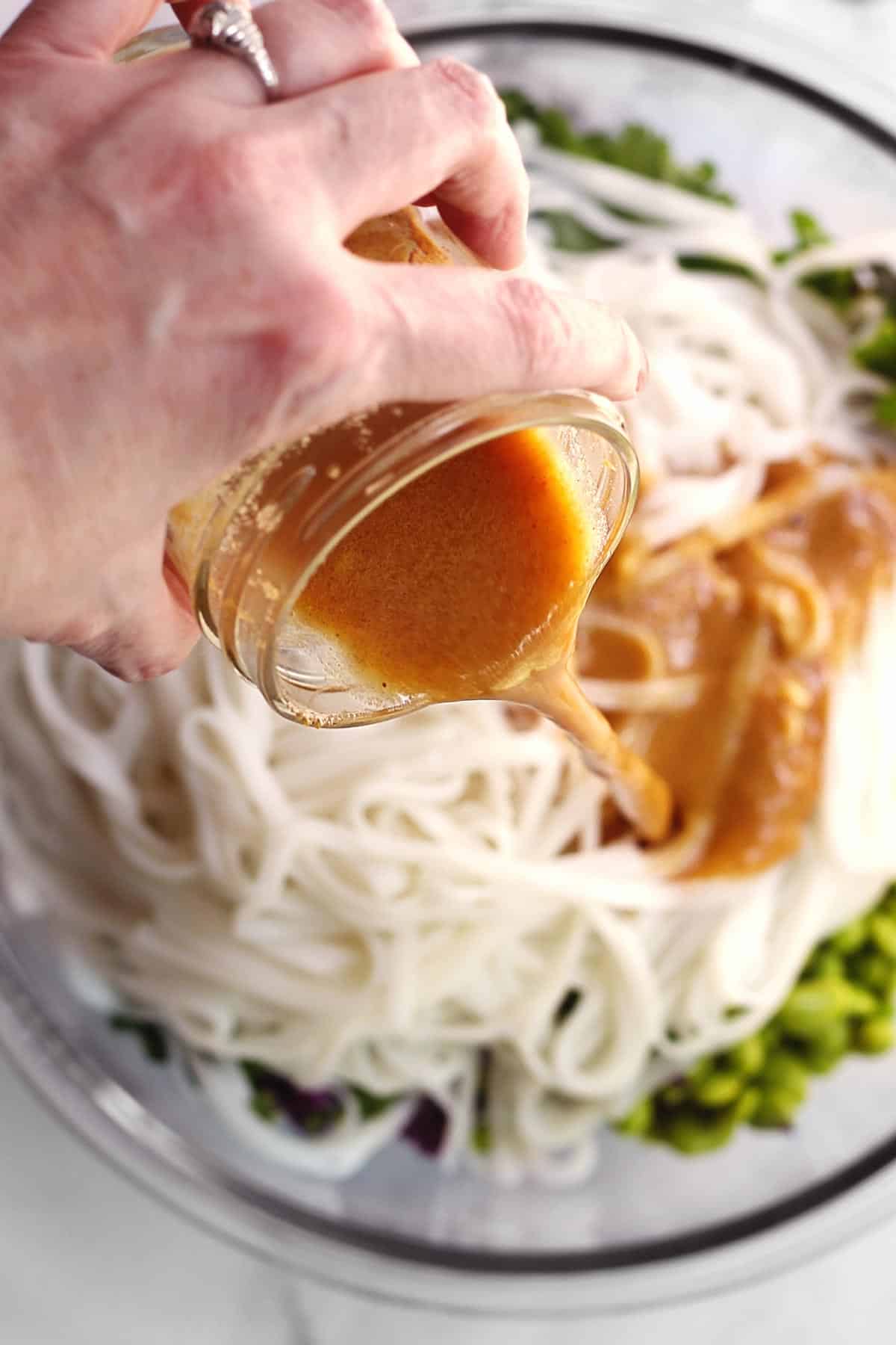 Peanut sauce being poured over noodle salad