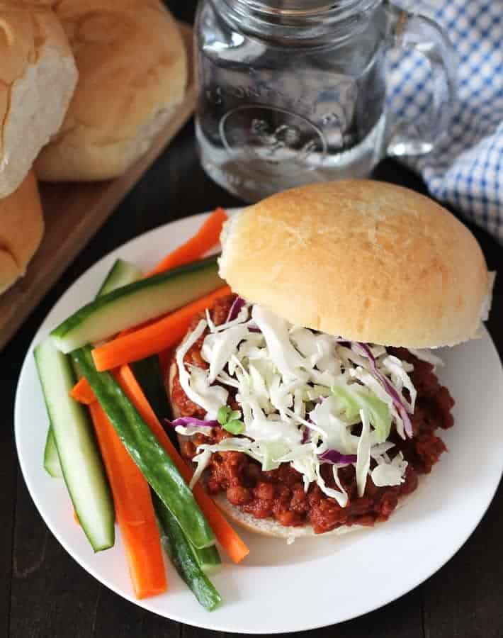 A picture of lentil sloppy joes with slaw with sliced veggies on a white plate