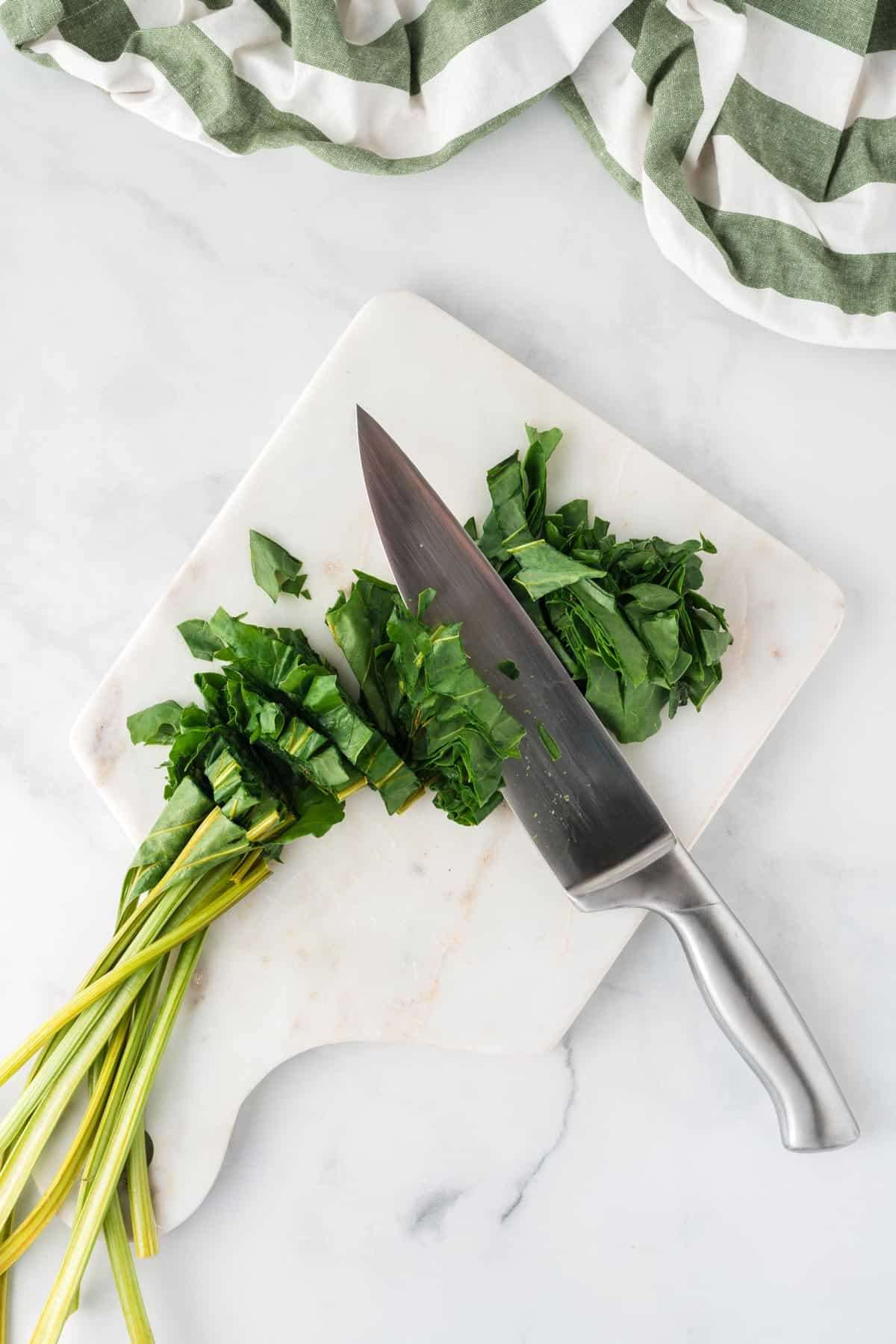 A picture of slicing beet greens with a knife on a white cutting board