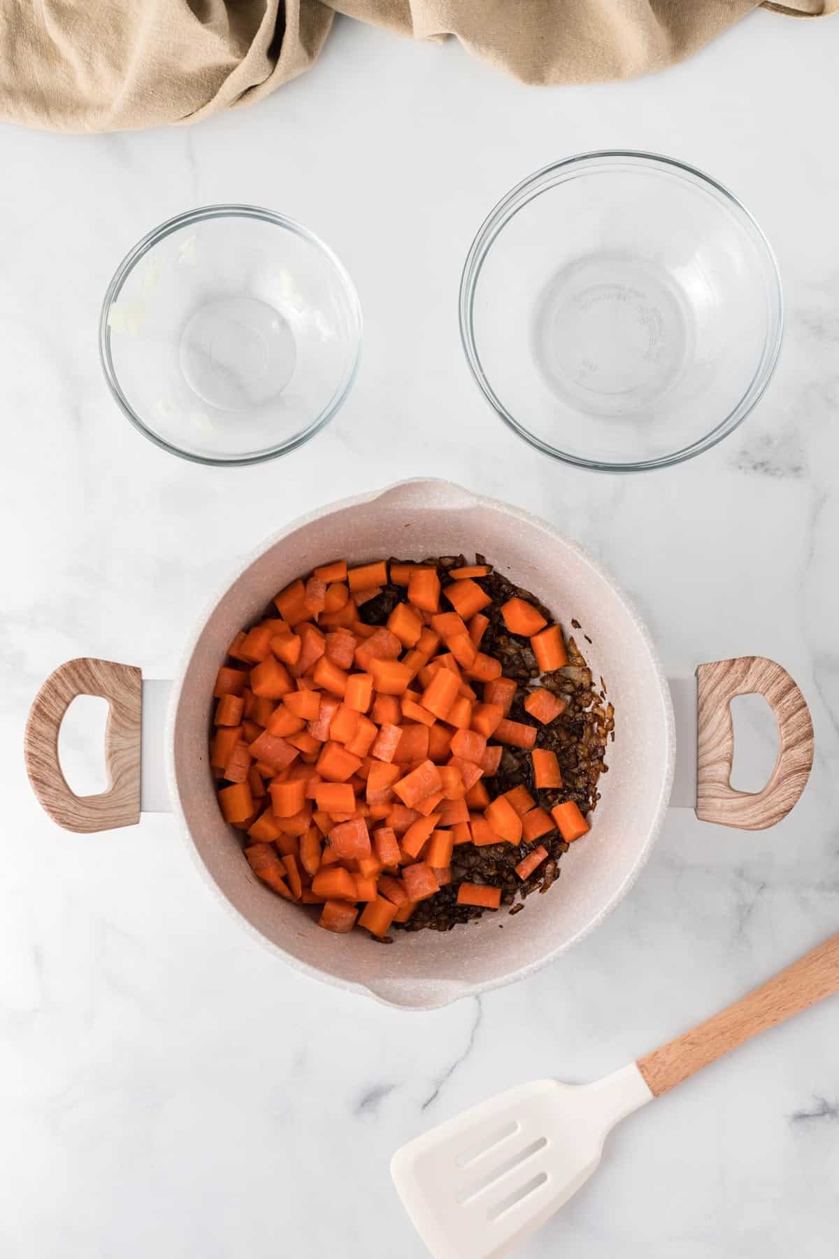 A picture of carrots and browned onions in a pot with two empty glass bowls next to it.