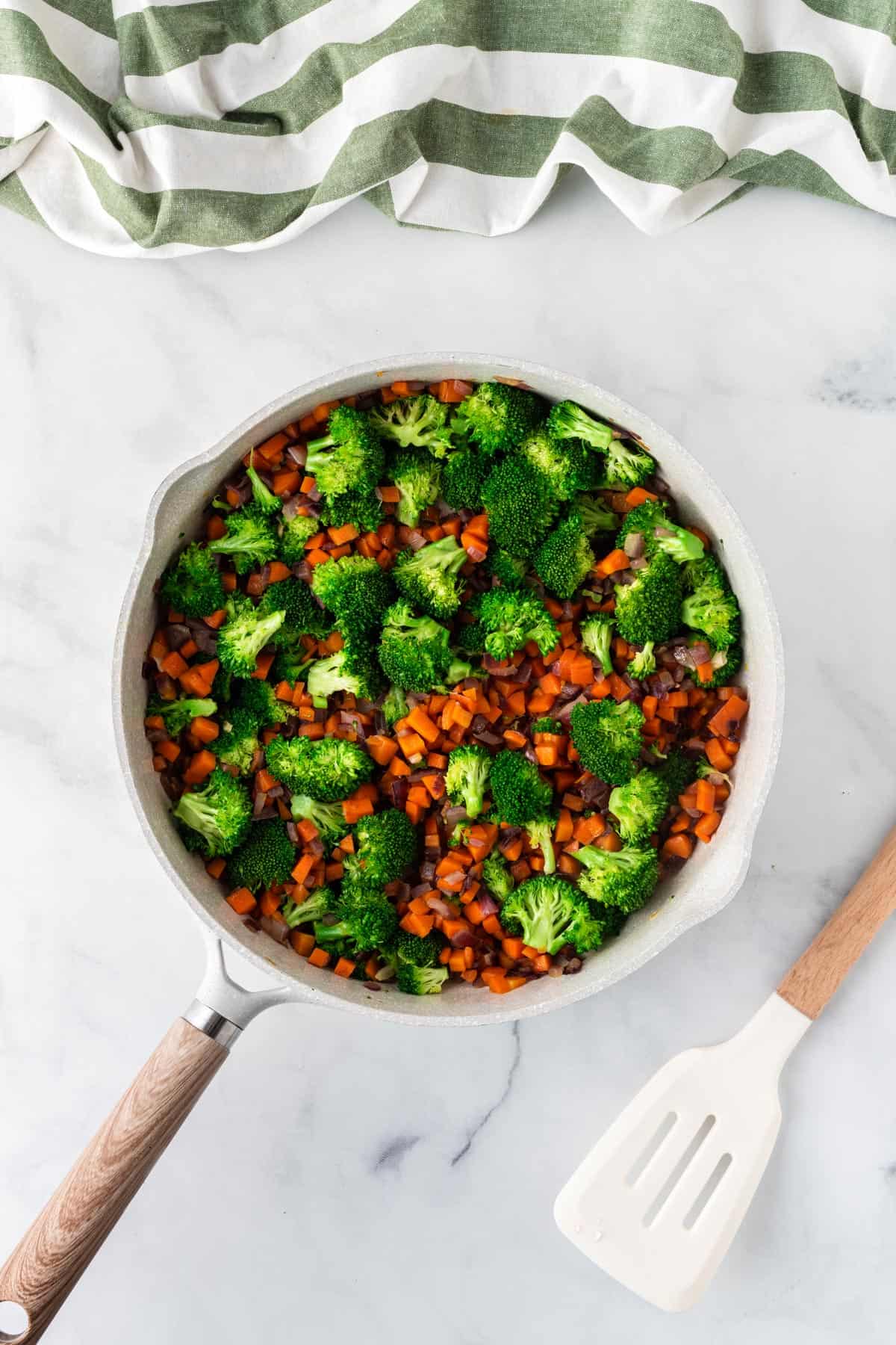 A picture of cooked broccoli, carrot, and red onion in a sauce pan.