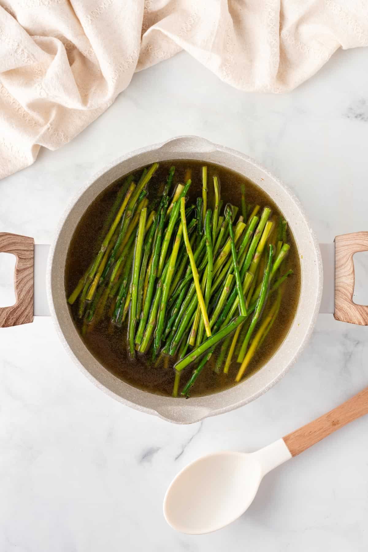 A picture of asparagus stalks cooking in broth in a pot.