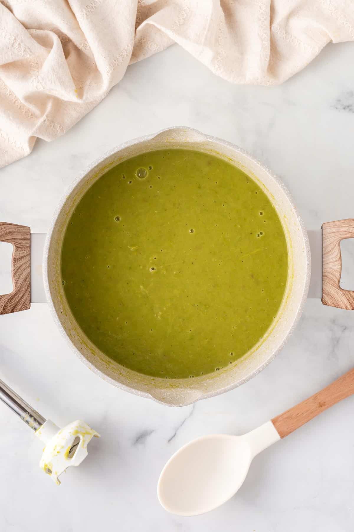 A picture of green asparagus soup in a soup pot with wooden handles.