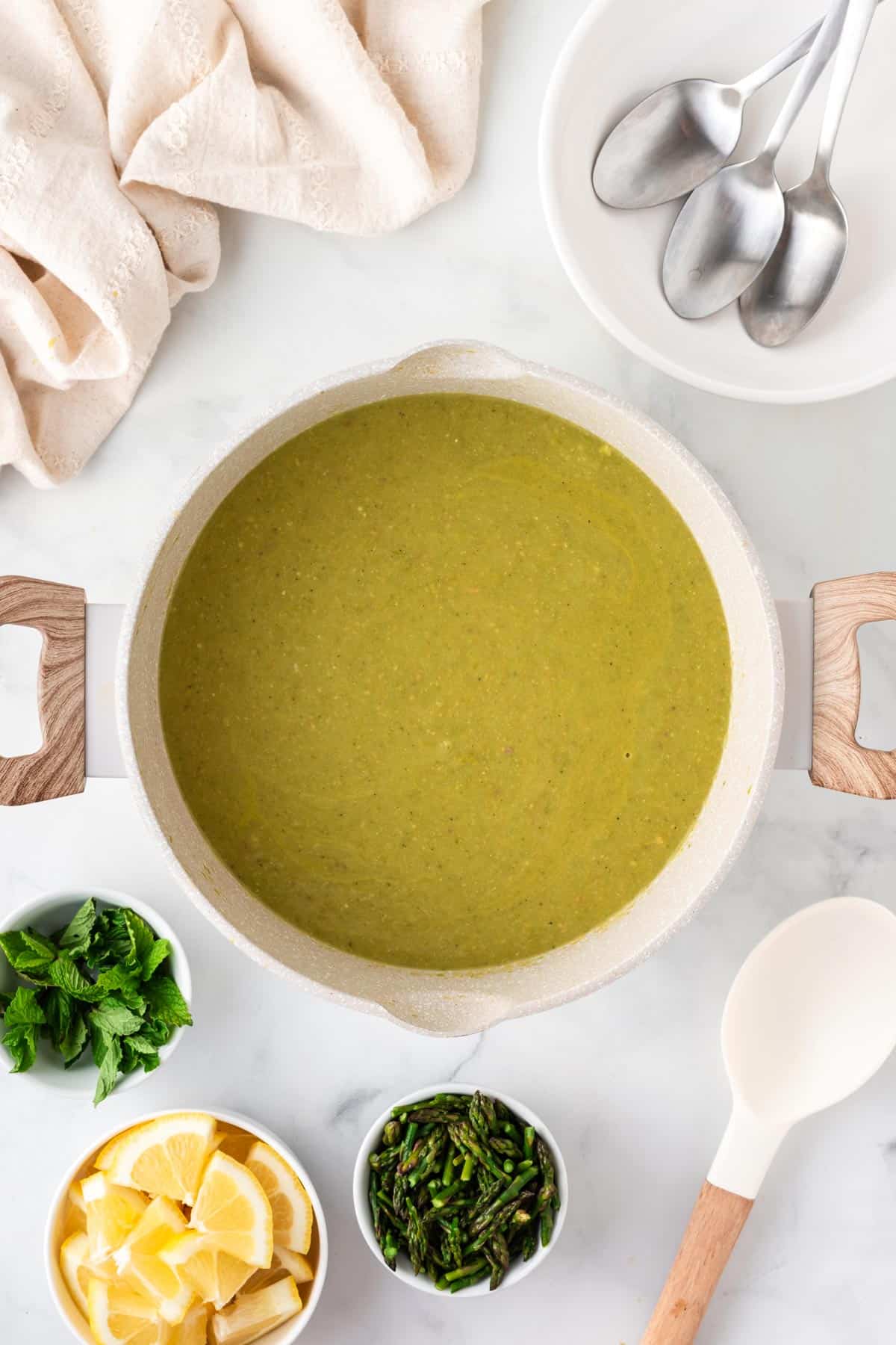 A picture of creamy asparagus soup in a pot with lemons, asparagus tips, and mint for garnish on the side.