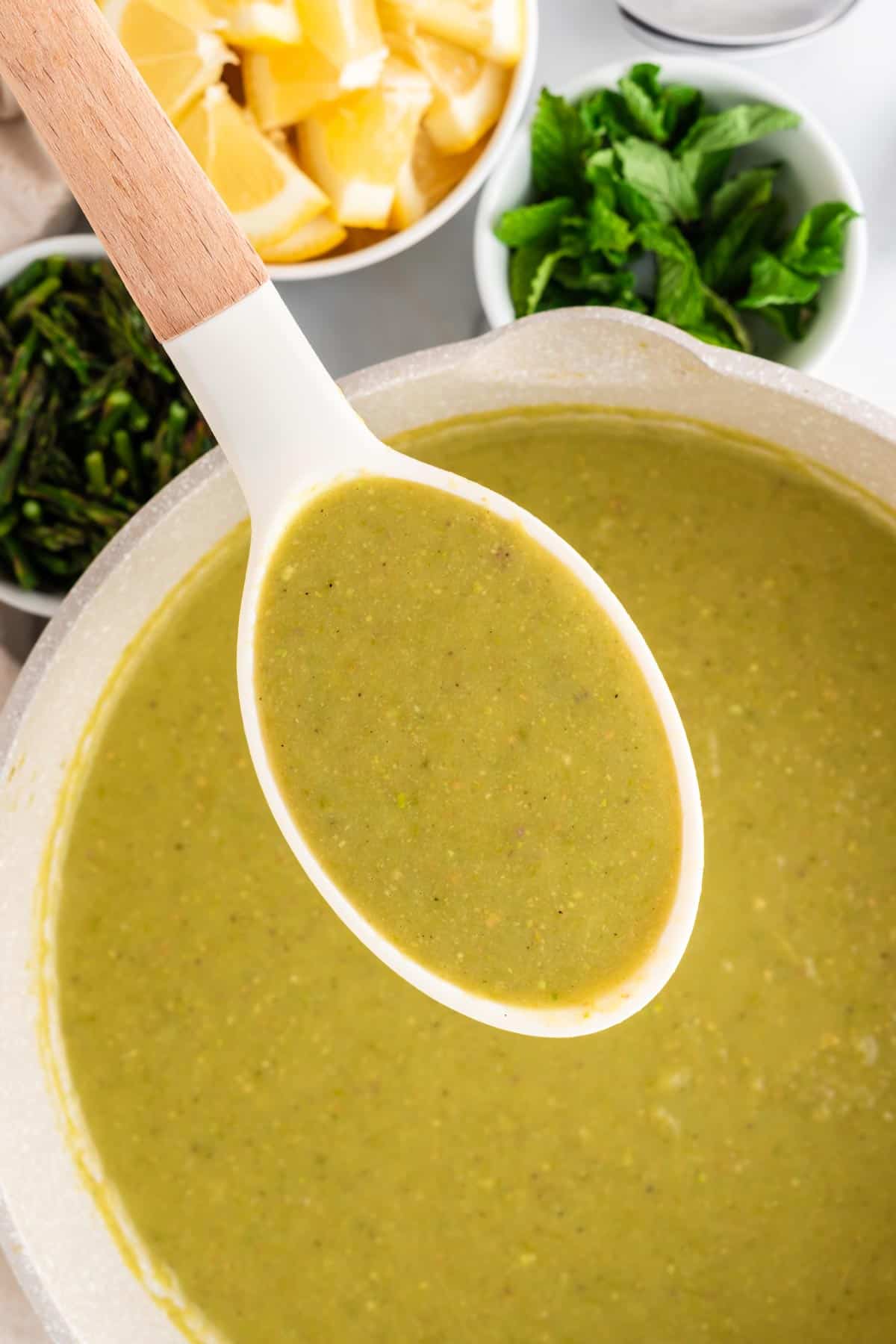 A picture of a white ladle ladling asparagus soup out of a cream colored pot.