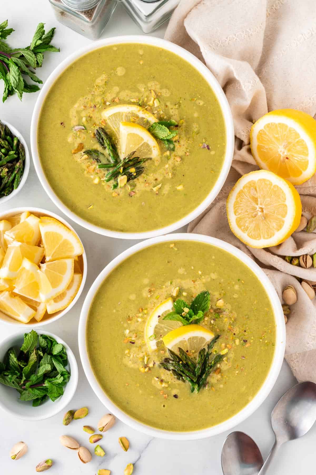 A picture of two bowls of asparagus soup with lemon, asparagus tips, and mint leaves for garnish.
