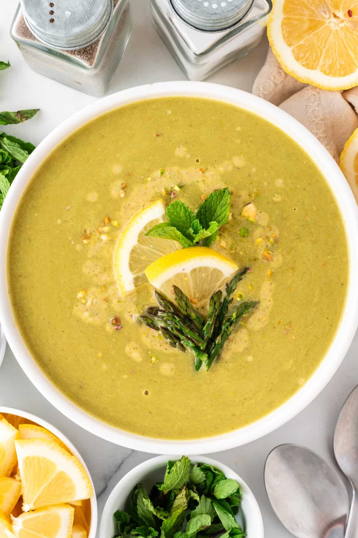 A picture of vegan asparagus soup with lemon, asparagus tips, and mint leaves on top.